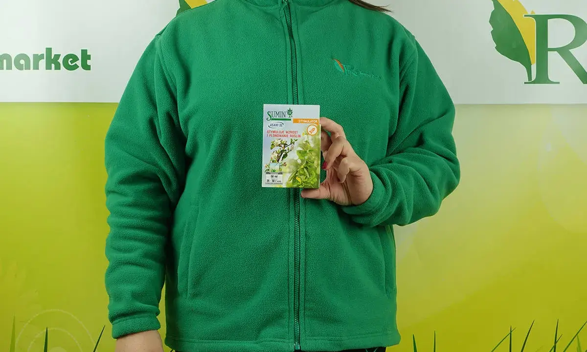 Kobieta w zielonej bluzie trzyma opakowanie stymulatora wzrostu roślin Asahi SL. Na opakowaniu widnieje informacja o dawkowaniu.