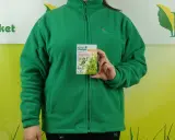 Kobieta w zielonej bluzie trzyma opakowanie stymulatora wzrostu roślin Asahi SL. Na opakowaniu widnieje informacja o dawkowaniu.
