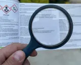 Lupa powiększa etykietę produktu, gdzie widnieje napis "Uwaga" i ostrzeżenia. Widać fragment instrukcji dotyczącej **dursban dawkowanie**.