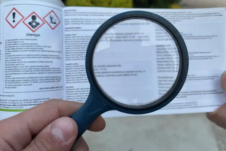 Lupa powiększa etykietę produktu, gdzie widnieje napis "Uwaga" i ostrzeżenia. Widać fragment instrukcji dotyczącej **dursban dawkowanie**.